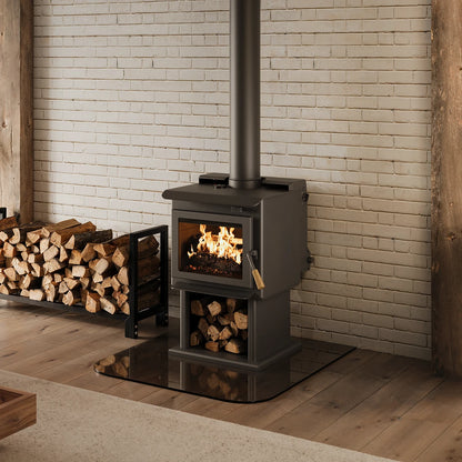 Small Blaze King Wood-burning stove with flames inside, surrounded by stacked logs against a brick wall.